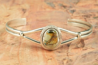 Genuine Boulder Turquoise set in Sterling Silver Bracelet. The cabochon is Boulder Turquoise, you can see the veins of Turquoise running through the host rock. The Boulder Turquoise Mine is located in northeast Nevada. It was discovered in 1970 by a Shoshone sheep herder. Production is small due to the remote location and winter weather. Boulder Turquoise is valued for both it's beauty and rarity. Every stone is unique. Created by Navajo Artist Lucy Valencia. Signed L. J. by the artist.